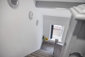 A staircase with a handrail, a small window with a view of the outside, and a wall-mounted decorative item. - 3 Bedroom With Backyard 10 Min to City Centre (Newcastle-upon-Tyne)