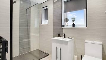Un baño moderno con cabina de ducha de vidrio, un lavamanos blanco con pomos negros y un inodoro.