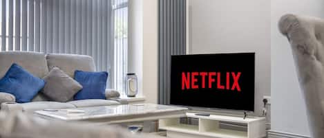 A living room with a sofa, a coffee table, and a TV displaying the Netflix logo.