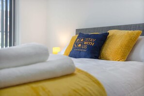 A neatly made bed with a white comforter and two pillows, one blue and one yellow, with a message on the blue pillow. - 3 Bedroom With Backyard 10 Min to City Centre (Newcastle-upon-Tyne)