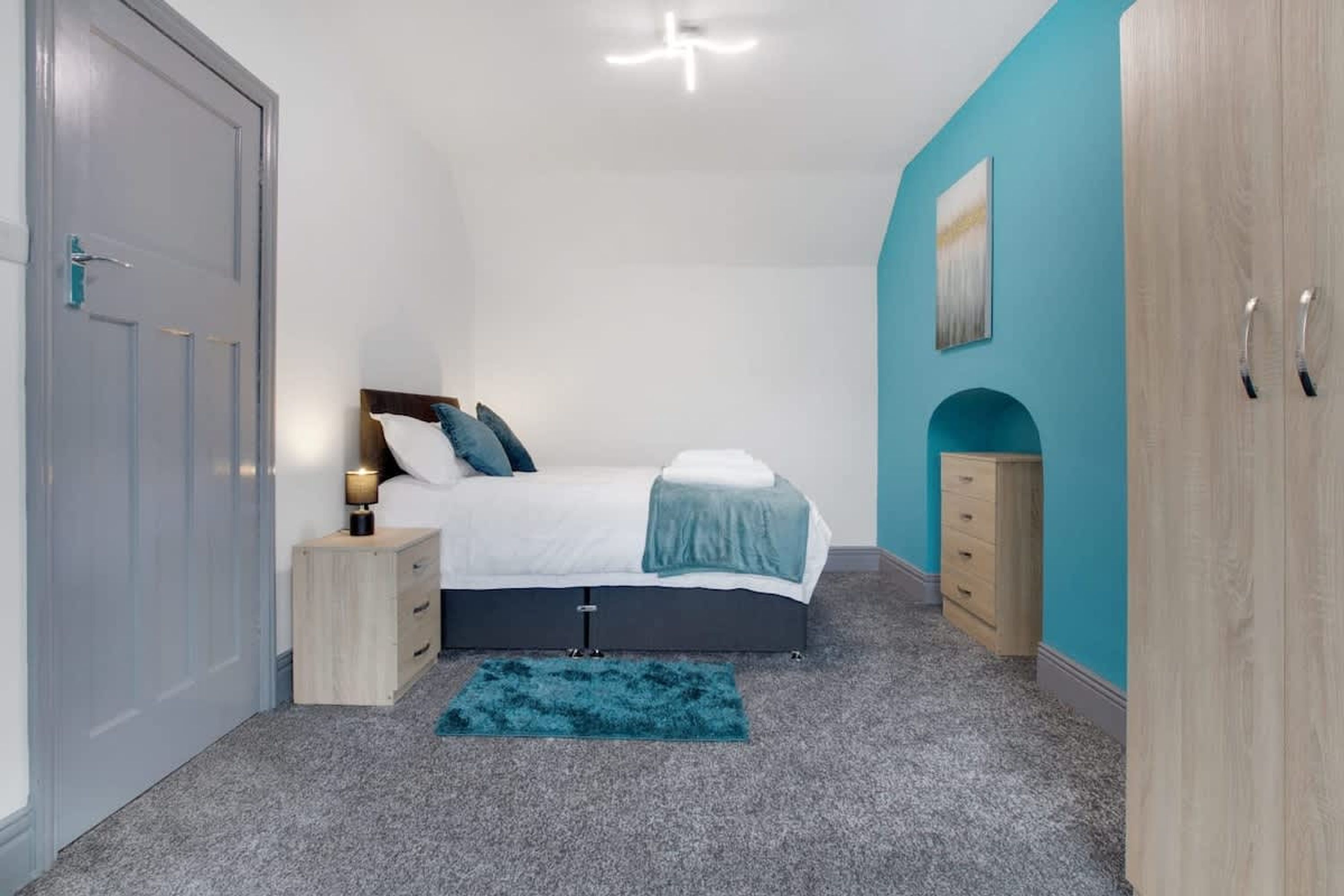 A bedroom with a bed, bedside tables, a dresser, and a door.