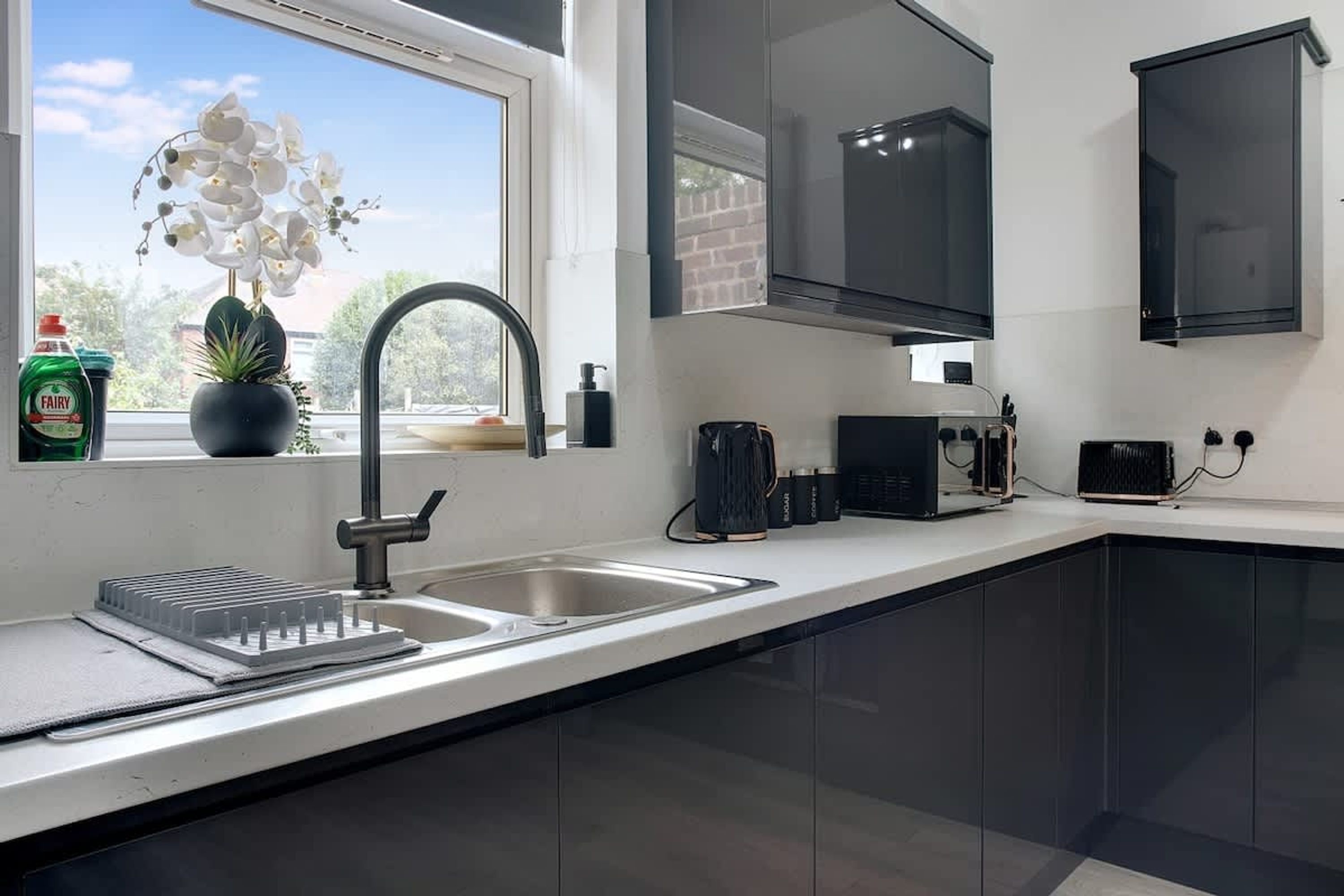 A modern kitchen with a stainless steel sink, a potted plant, and a window with a view of greenery.