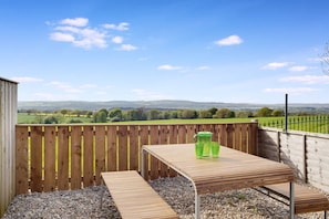 A wooden deck with a table and benches, overlooking a rural landscape with fields and hills. - Two Bedroom Family Home With Garden Field View (Durham)