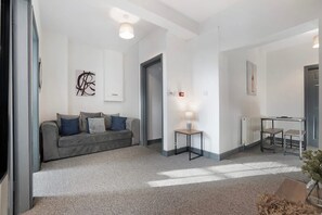 Ein modernes Wohnzimmer mit einem grauen Sofa, einem kleinen Tisch und einem Bild an der Wand.