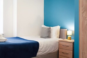 Ein Schlafzimmer mit einem Bett, einem Nachttisch, einer Lampe und einem Fenster.