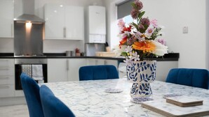Una cucina moderna con mobili bianchi, una cappa aspirante in acciaio inossidabile e un'area pranzo con una sedia blu e un vaso di fiori su un tavolo in marmo.