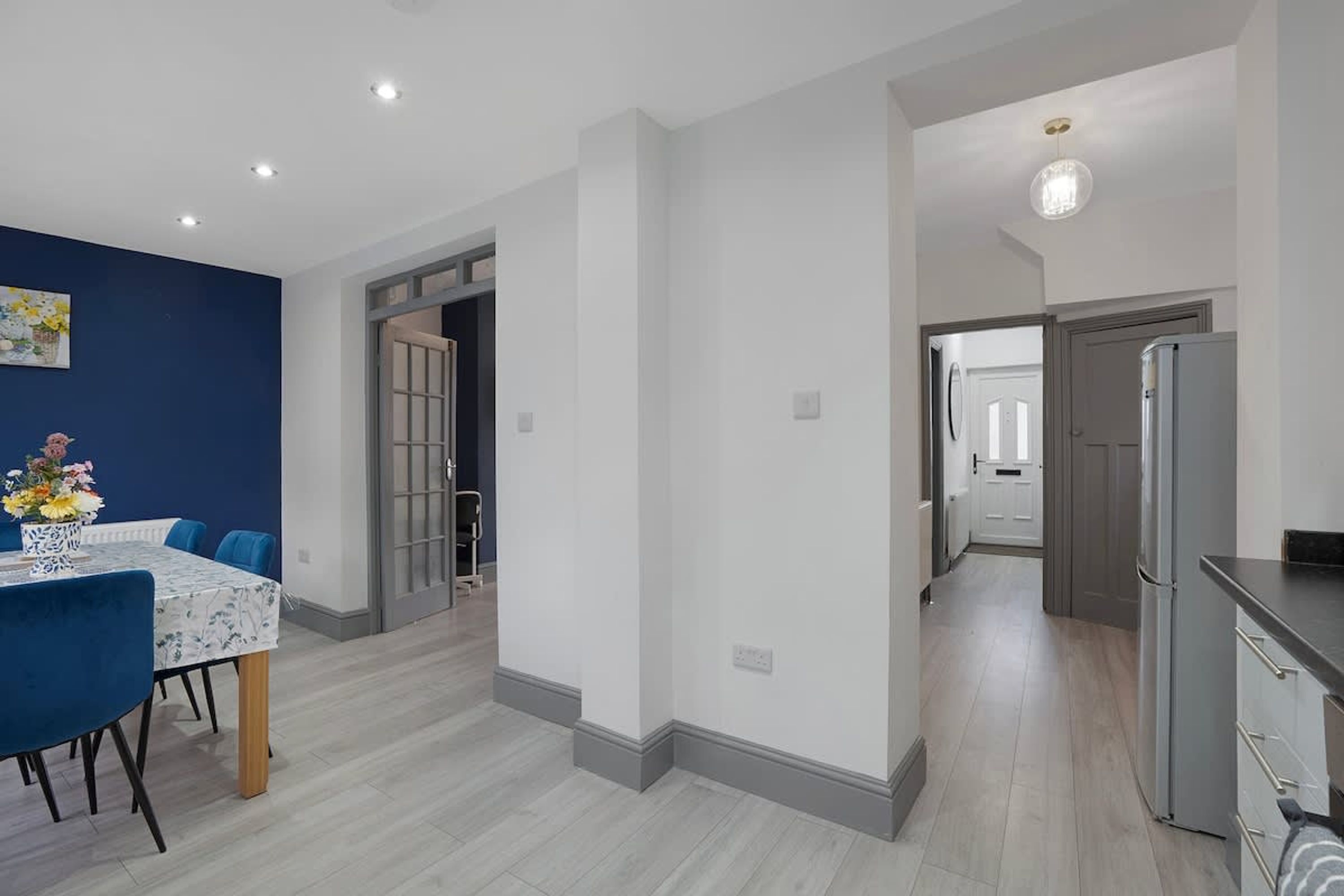 A modern kitchen with a refrigerator, a dining area with a table and chairs, and a hallway leading to another room.