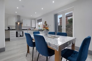 A modern kitchen with white cabinets, a central island, and a dining area with blue chairs and a marble table. - Newcastle 2BR Sleeps 5 2 Parking by Stay With Us (Newcastle-upon-Tyne)