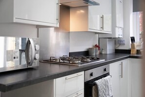 Een moderne keuken met een gasfornuis, witte kastjes en een roestvrijstalen koelkast.