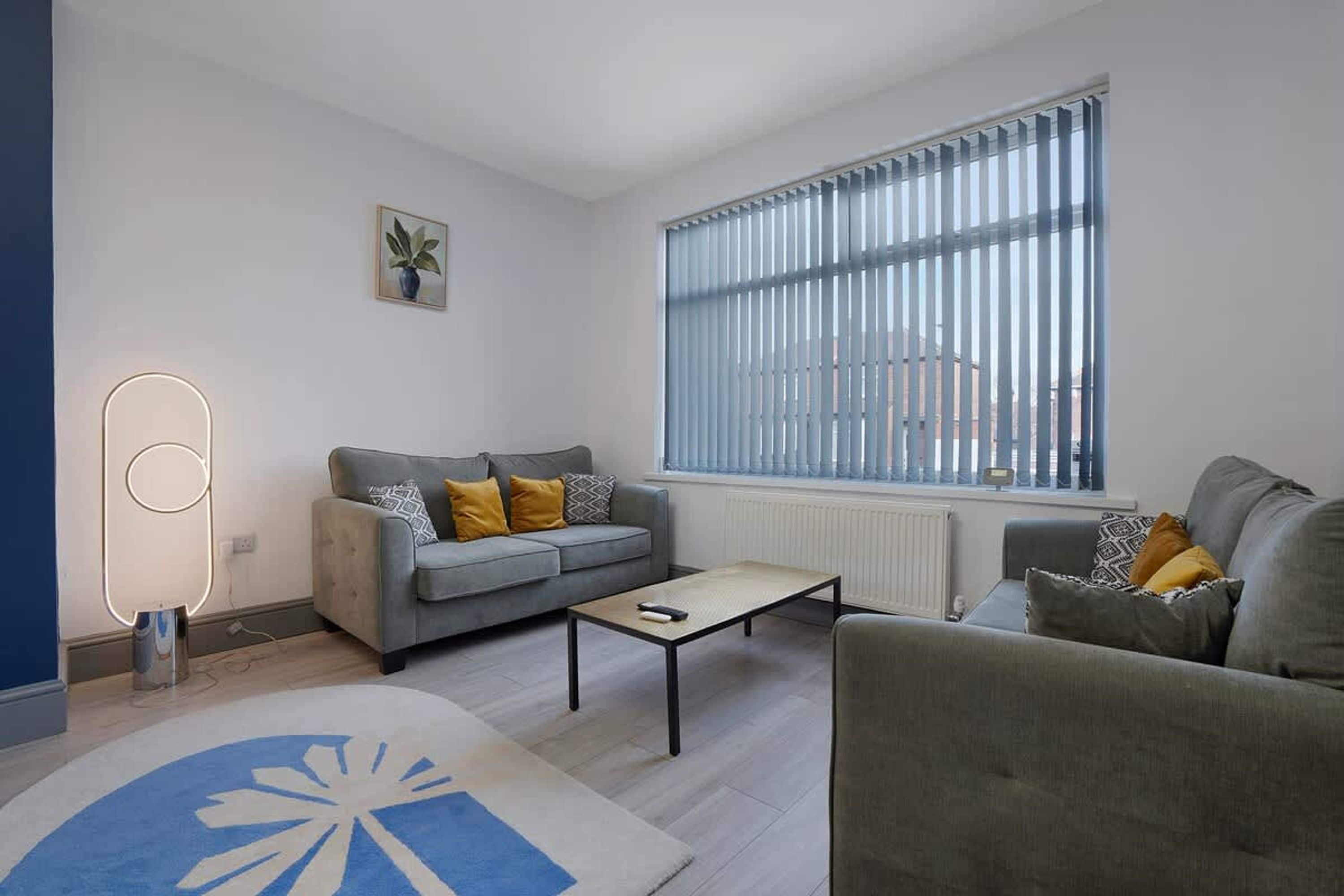 A modern living room with a grey sofa, a coffee table, and a large window with blinds.