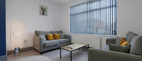 Una sala de estar moderna con un sofá gris, una mesa de centro y un ventanal con persianas.