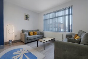 A modern living room with a grey sofa, a coffee table, and a large window with blinds. - Newcastle 2BR Sleeps 5 2 Parking by Stay With Us (Newcastle-upon-Tyne)