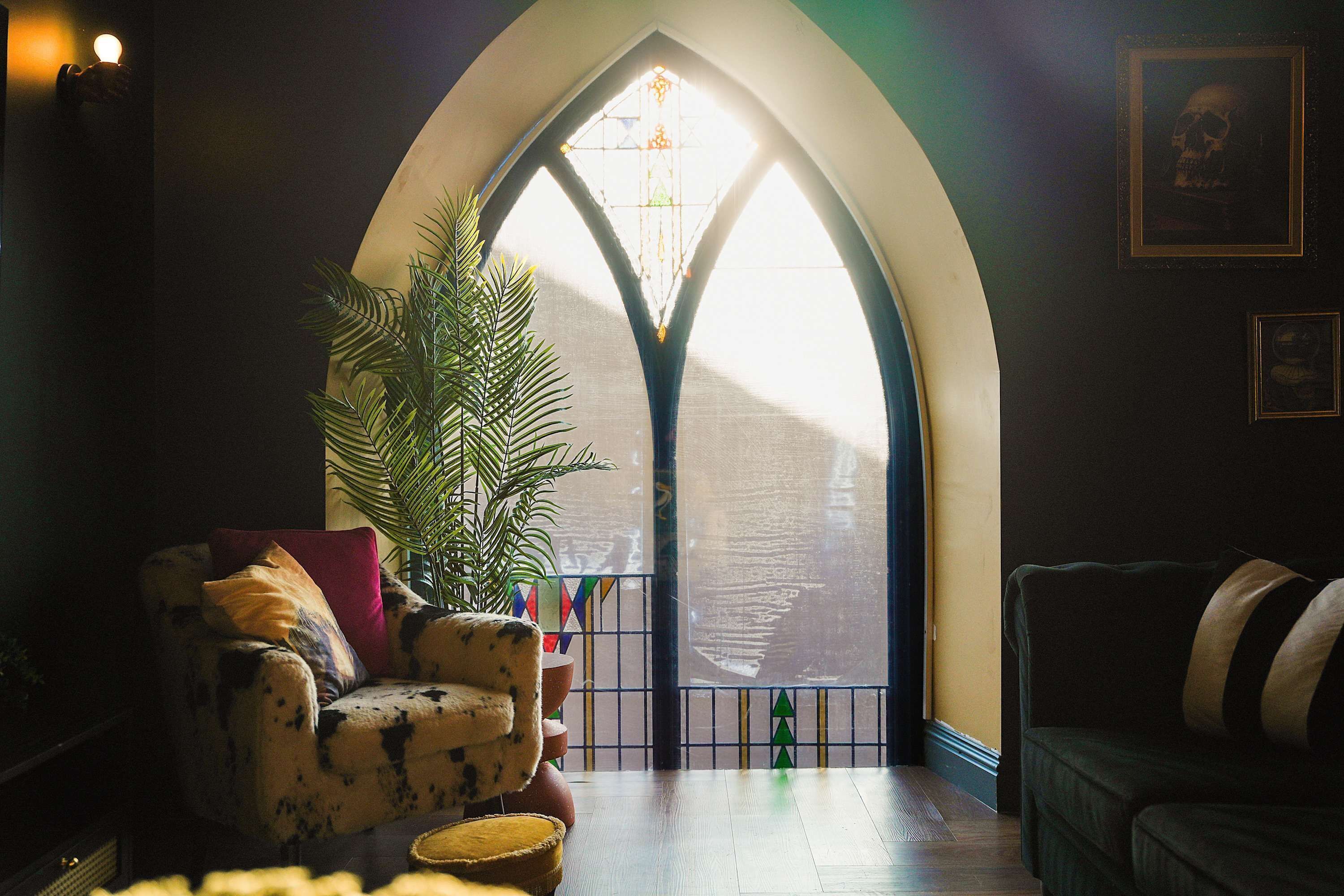 A cozy living room with a large arched window, a potted plant, and a patterned armchair.