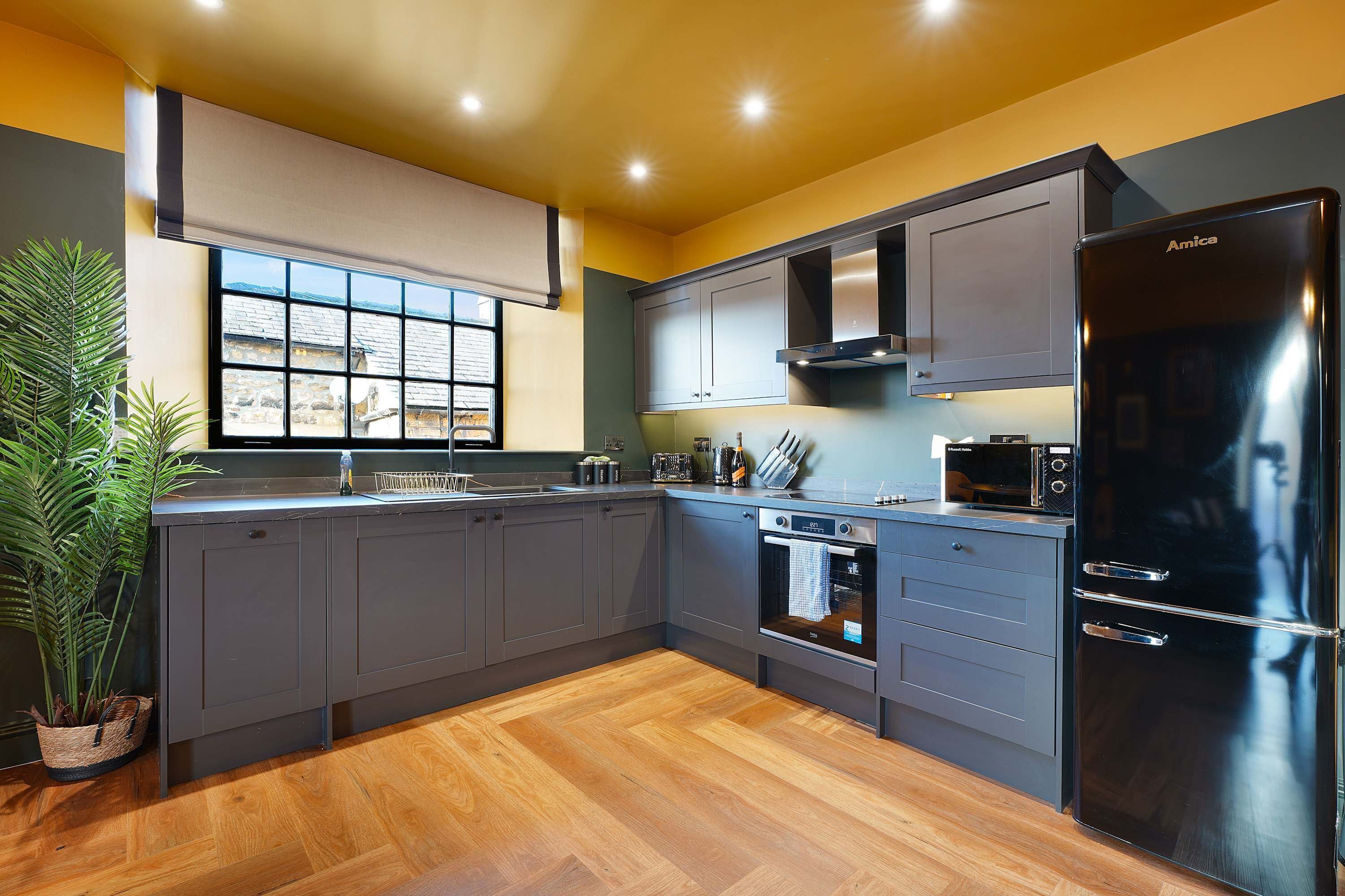A modern kitchen with grey cabinets, a black refrigerator, and a window with a view of a house.