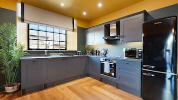 A modern kitchen with grey cabinets, a black refrigerator, and a window with a view of a house.