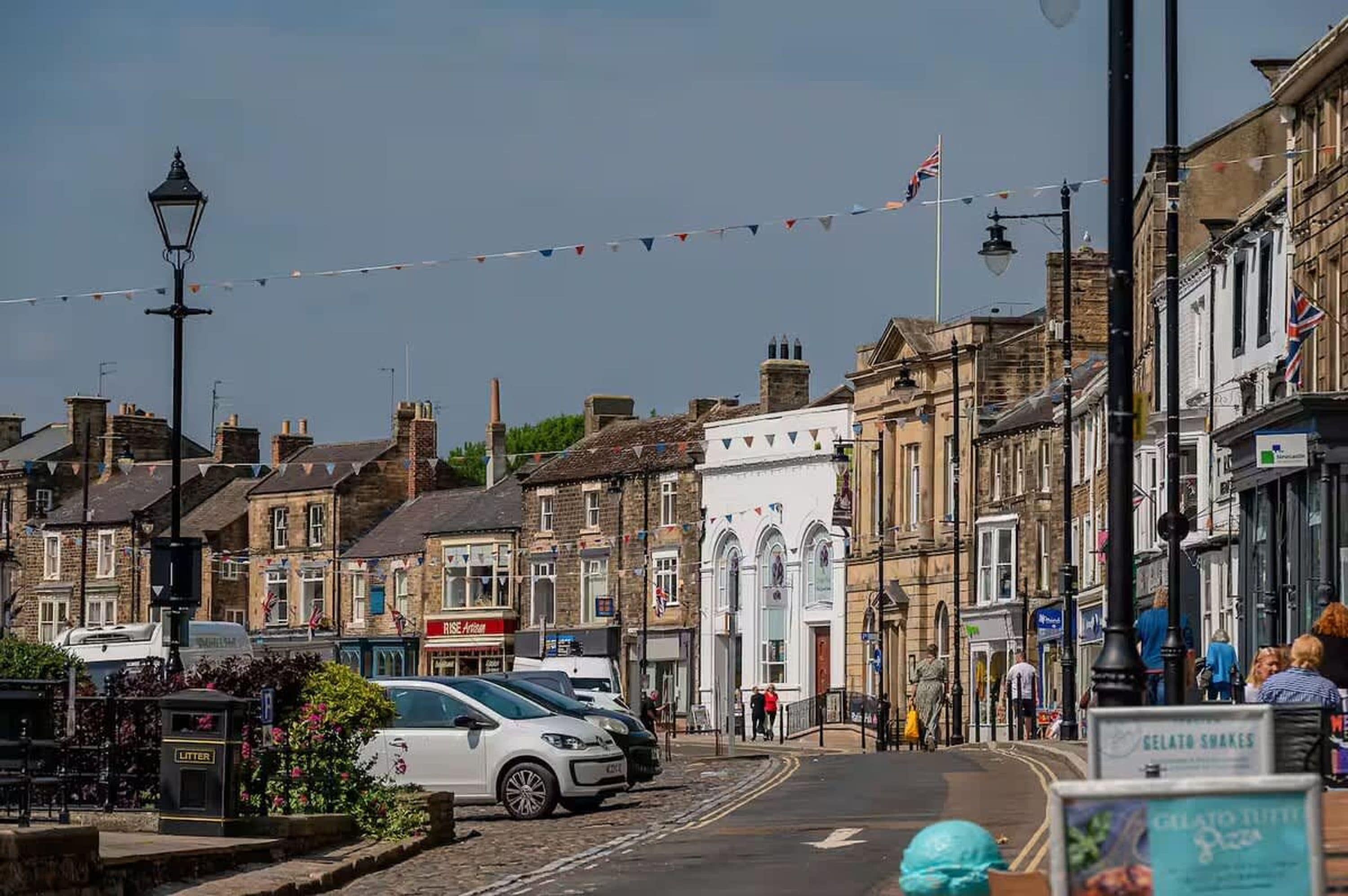 A street lined with traditional buildings, a parked car, and a shop with a sign.
