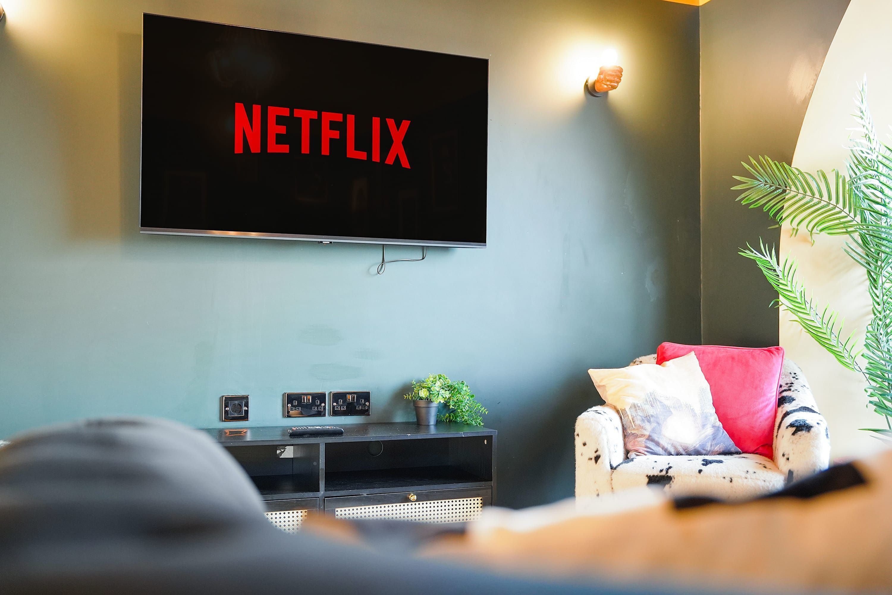 A living room with a flat-screen TV mounted on the wall displaying 'NETFLIX' in red letters.