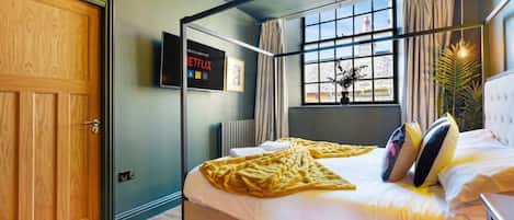 A hotel room with a bed, a television mounted on the wall, a window with curtains, and a chandelier.
