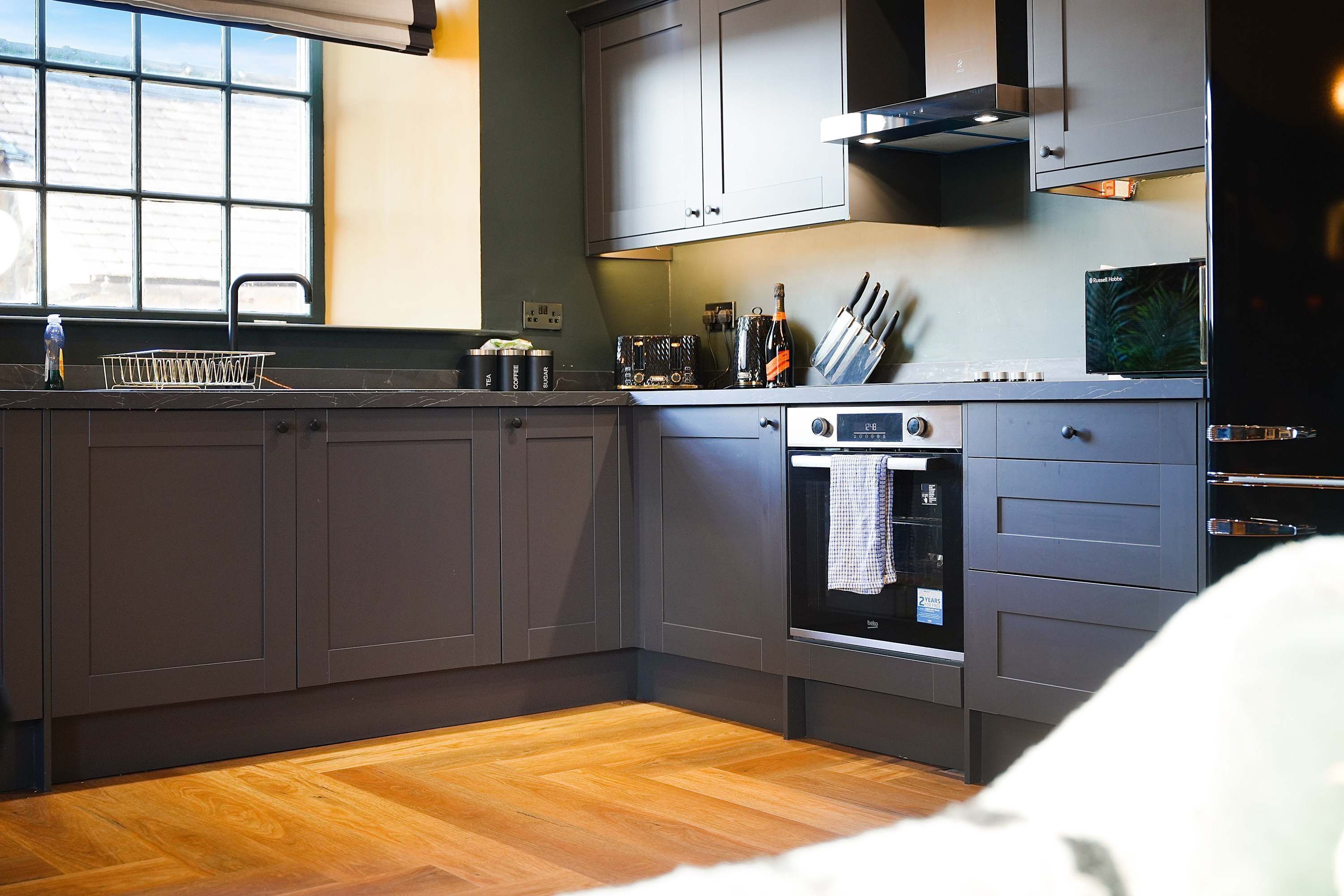 Una cocina moderna con gabinetes grises, horno integrado y ventana con vistas al exterior.