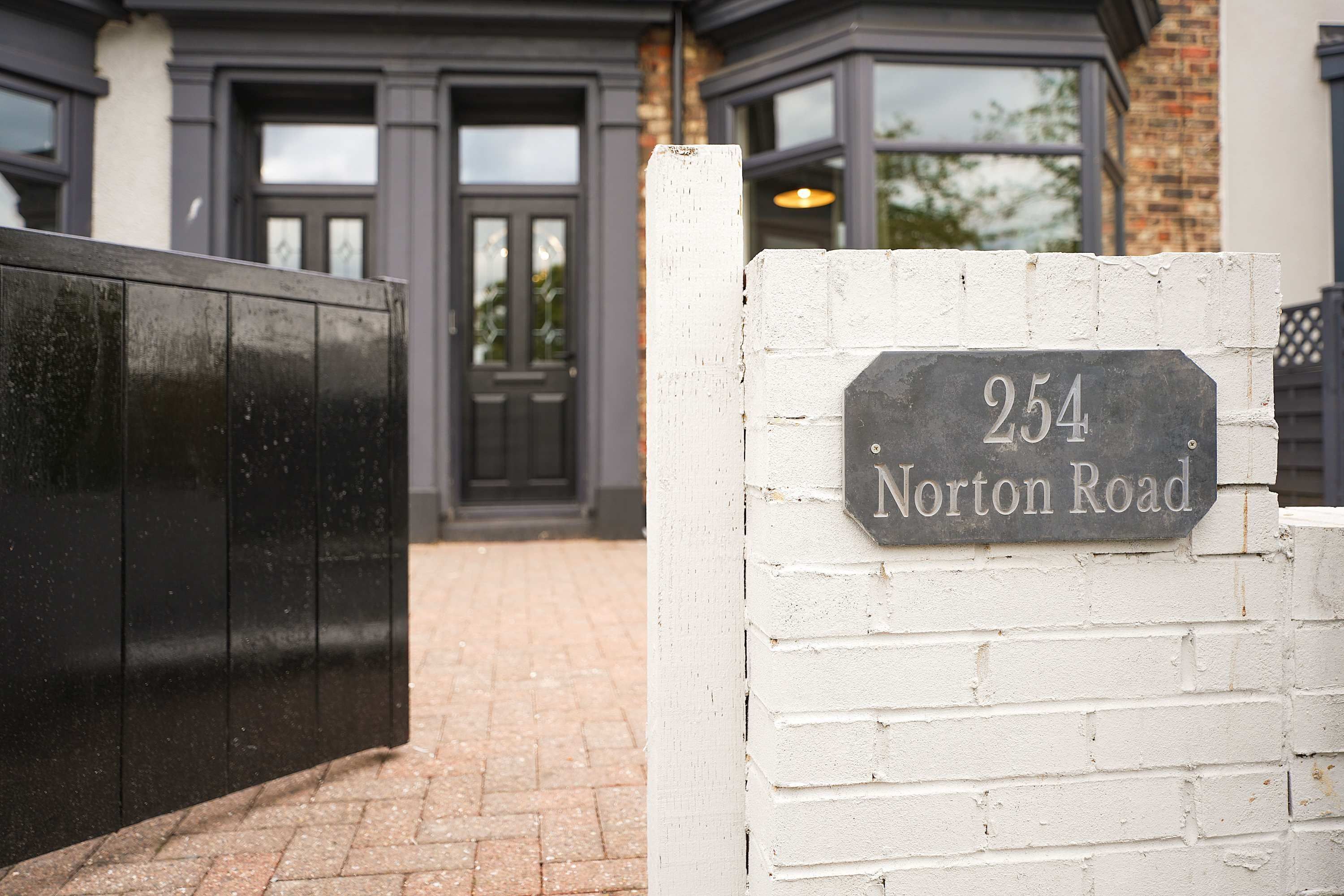 A house number sign on a white brick wall, indicating '254 Norton Road.'
