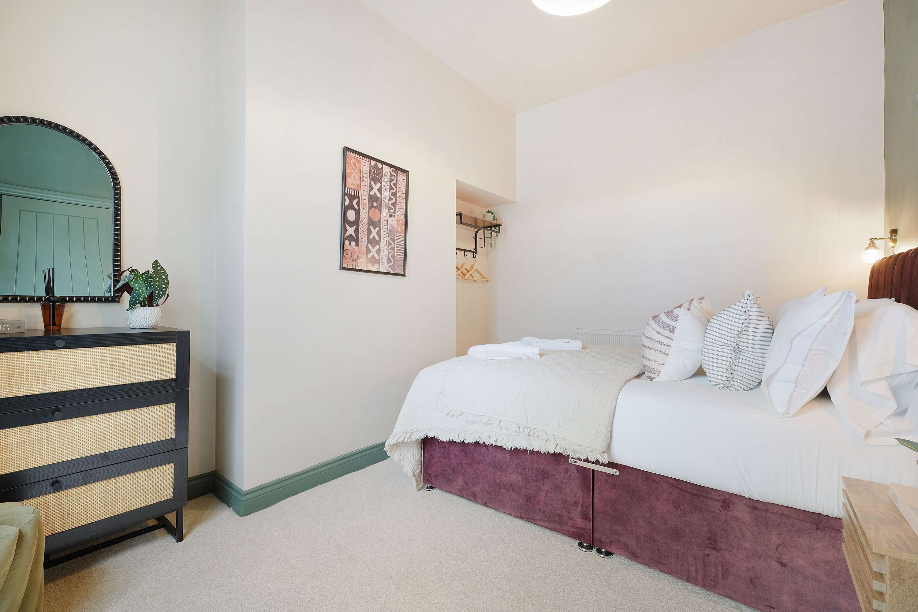 Een slaapkamer met een bed, een dressoir, een spiegel, een kunstwerk aan de muur en een deur naar een andere kamer.