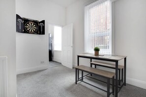 A room with a dartboard, a window with blinds, a bench, and a small table with a plant. - Spacious Home for Groups Contractors Free Wifi (Sunderland)