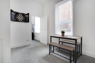 Una habitación con dardos, una ventana con persianas, un banco y una mesita con una planta.