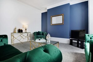 A living room with a blue accent wall, a large flat-screen TV, and green upholstered furniture. - Spacious Home for Groups Contractors Free Wifi (Sunderland)