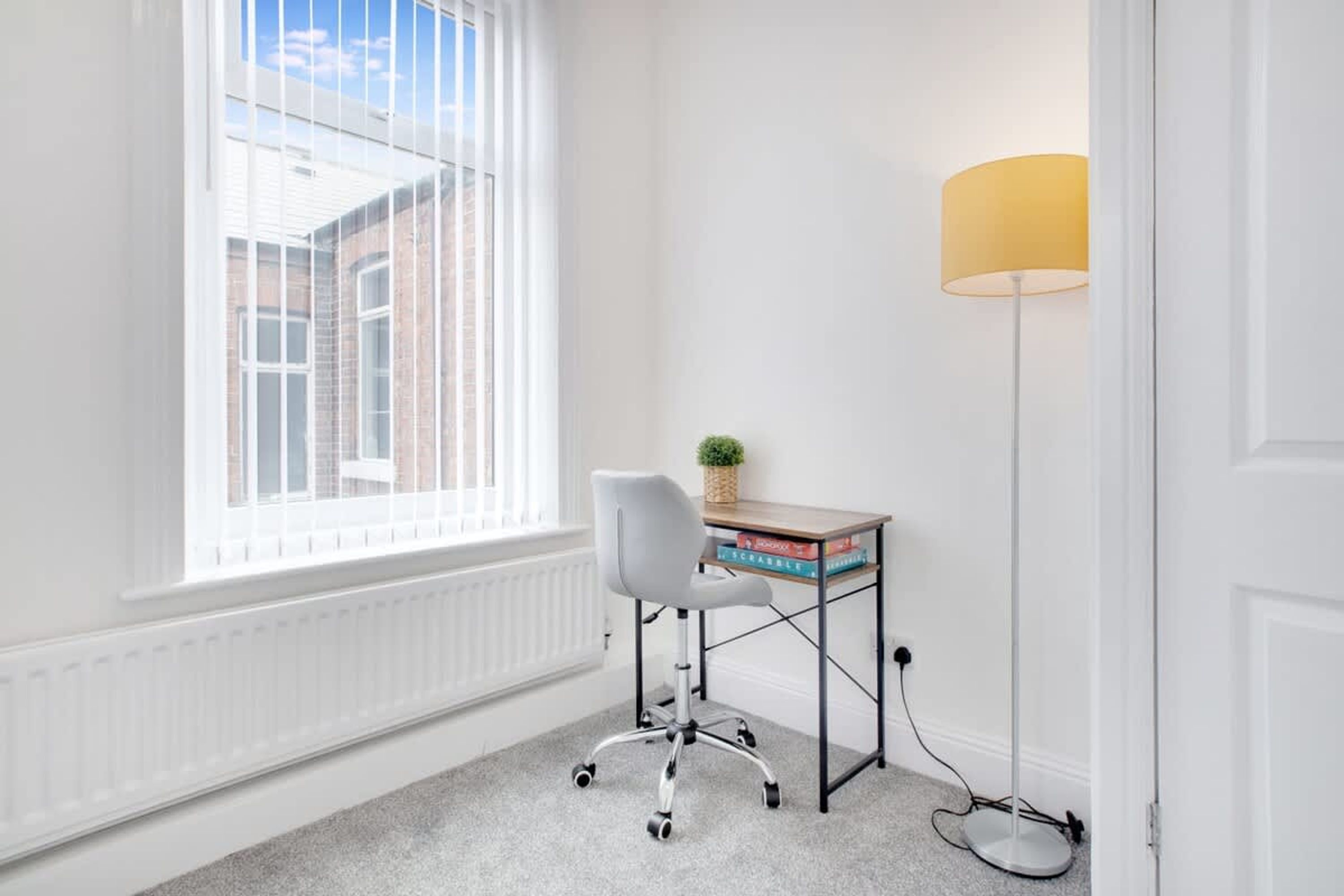 Una habitación con ventana, un escritorio con libros, una lámpara y una silla.