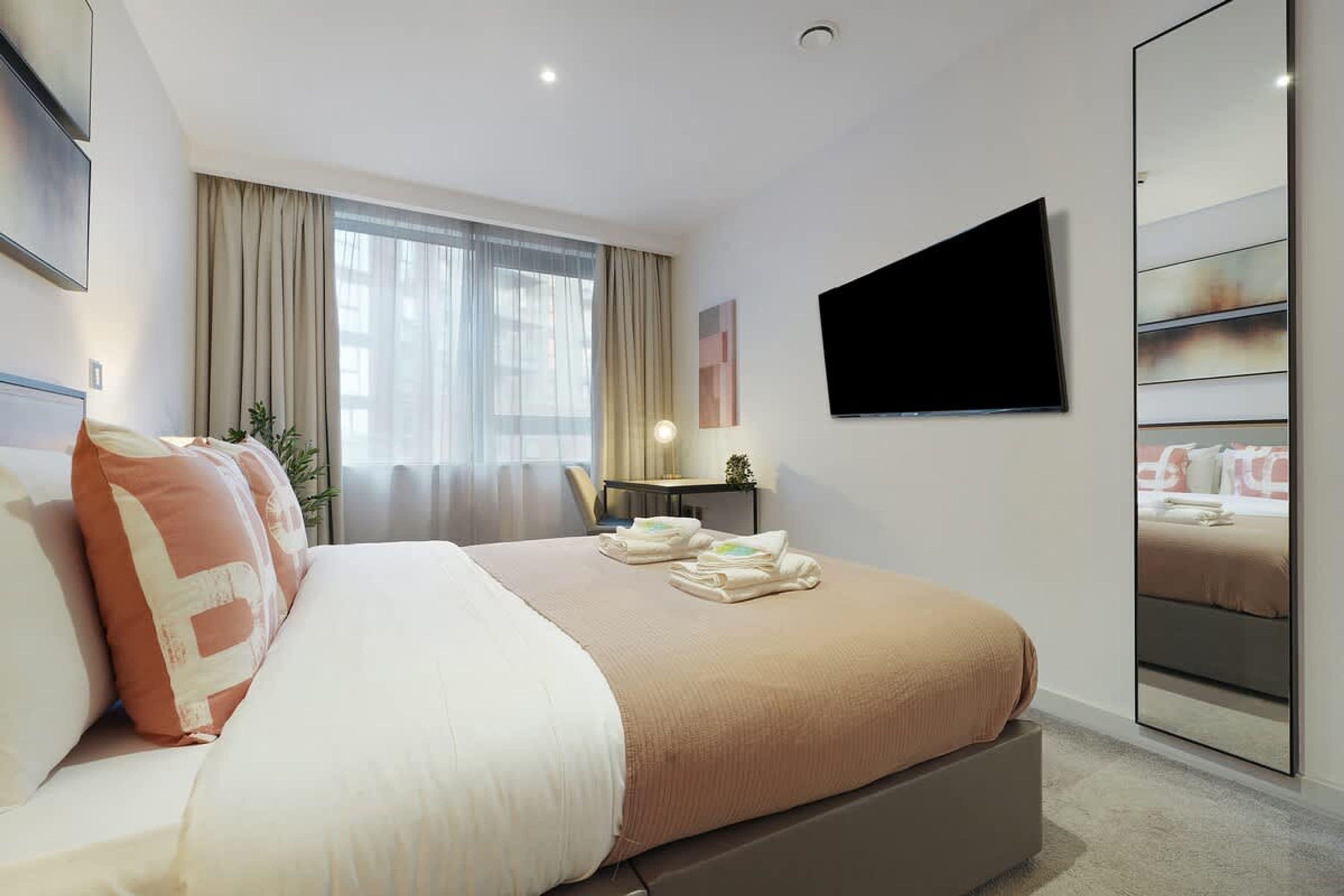 Habitación de hotel con cama, escritorio, silla, televisor y armario.