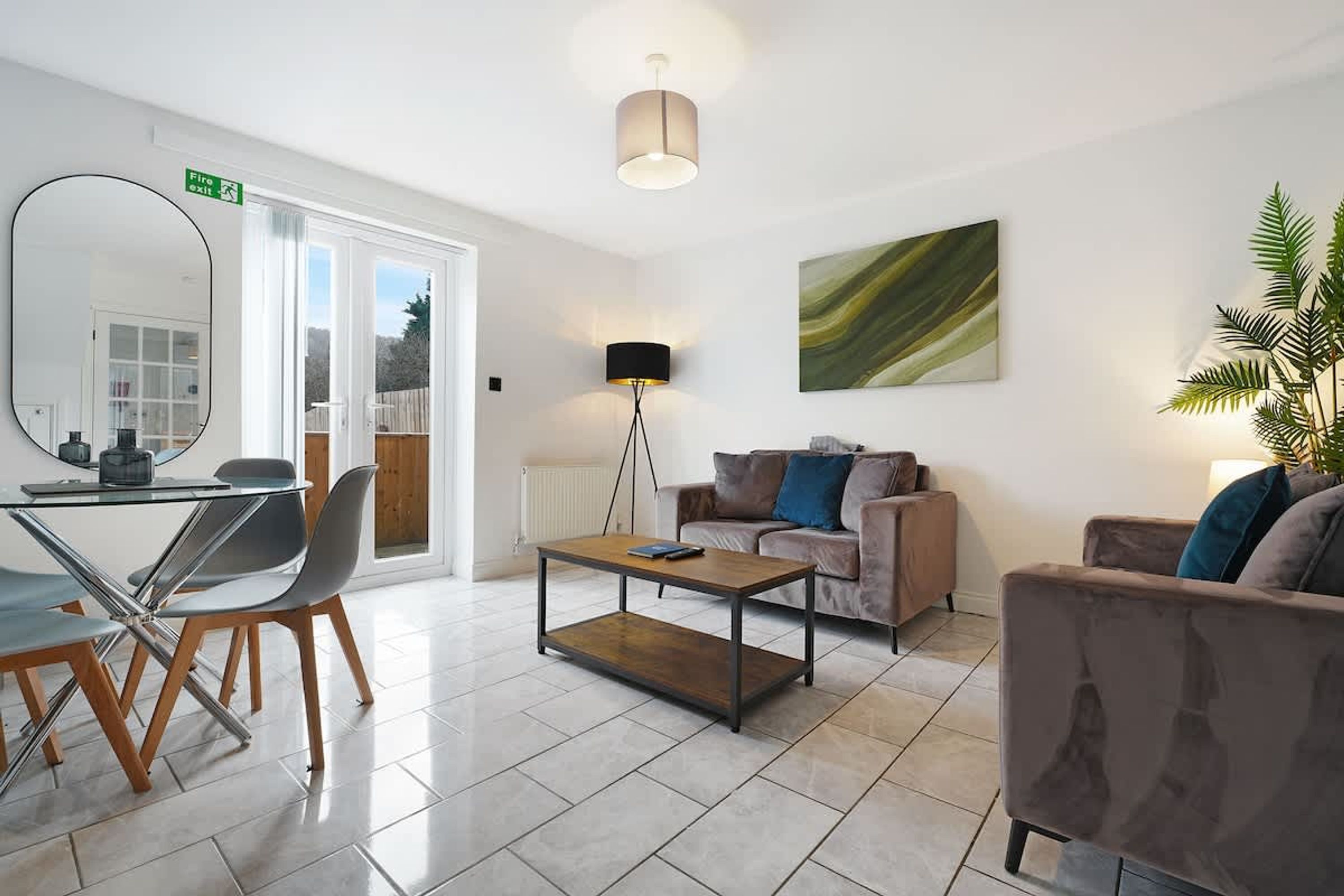 A modern hotel lobby with a dining area, a sofa set, a floor lamp, and a painting on the wall.