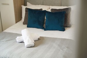 Ein ordentlich bezogenes Bett mit einem gemusterten Bettüberwurf, zwei Kissen und einem zusammengerollten Handtuch auf der Seite.