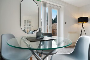 Ein moderner Essbereich mit einem Glastisch, zwei Stühlen, einer Flasche und einer Lampe.