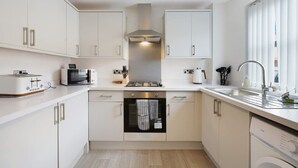 A compact kitchen with white cabinetry, a built-in oven, a microwave, and a gas stove. - Modern 3 Bed Home With Garden Free Parking Wi-fi (Middlesbrough)