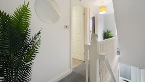 A hallway with a white door, a round mirror, and a staircase with a white railing. - Modern 3 Bed Home With Garden Free Parking Wi-fi (Middlesbrough)