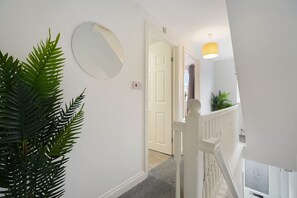 Ein Flur mit einer weißen Tür, einem runden Spiegel und einer Treppe mit weißer Geländer.
