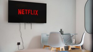 A modern room with a flat-screen TV mounted on the wall displaying 'NETFLIX' in red letters, a glass table with chairs, and a power outlet on the wall. - Modern 3 Bed Home With Garden Free Parking Wi-fi (Middlesbrough)