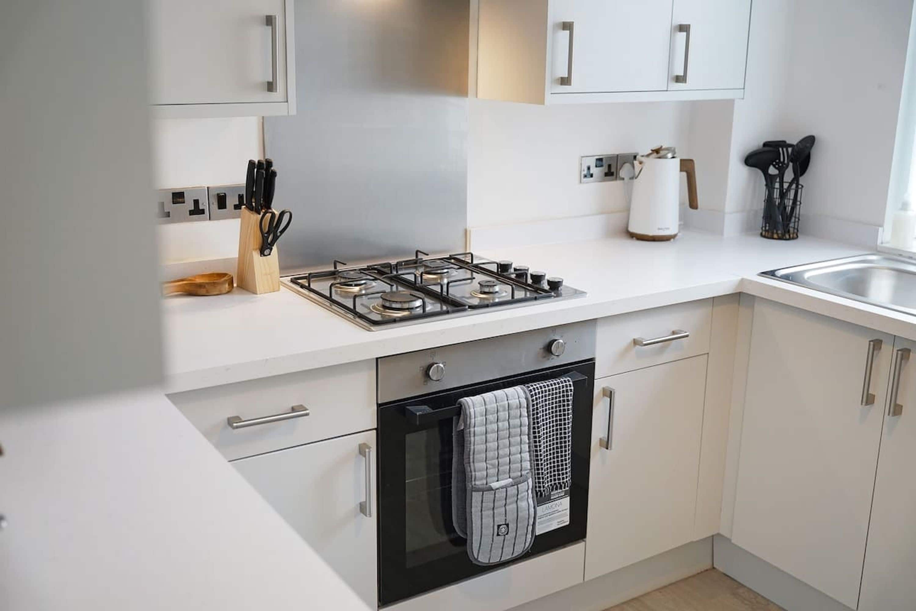 A modern kitchen with white cabinetry, a gas stove, an oven, and a coffee maker.