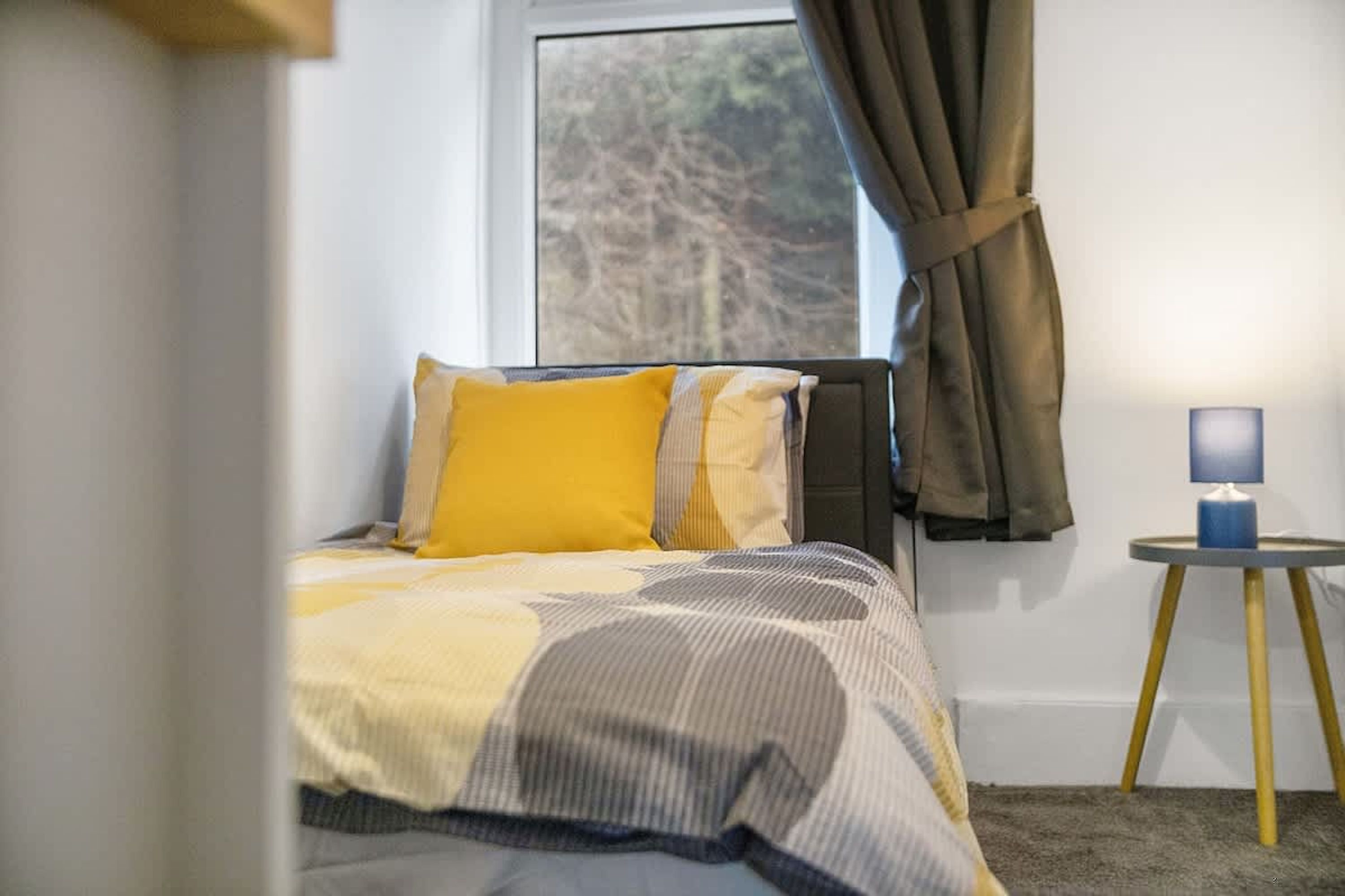 A bedroom with a bed, a nightstand, a lamp, and a window with curtains.