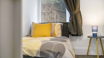 A bedroom with a bed, a nightstand, a lamp, and a window with curtains.