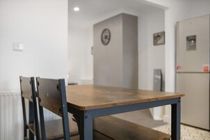 A dining table with chairs in a room with white walls, a radiator, and a door with a picture.