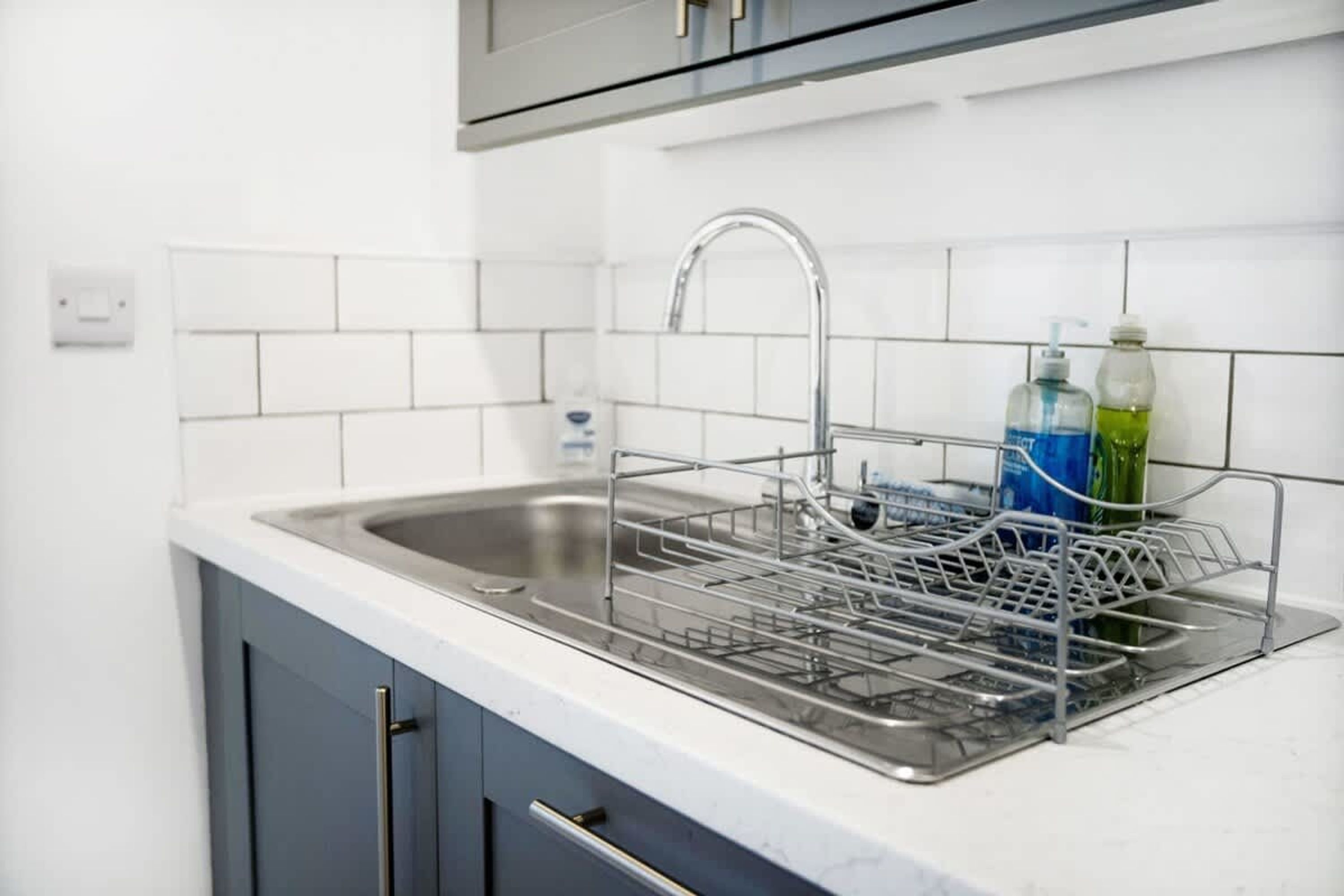 Una cucina con un lavello in acciaio inox, un portascopini e una bottiglia di detersivo per piatti.