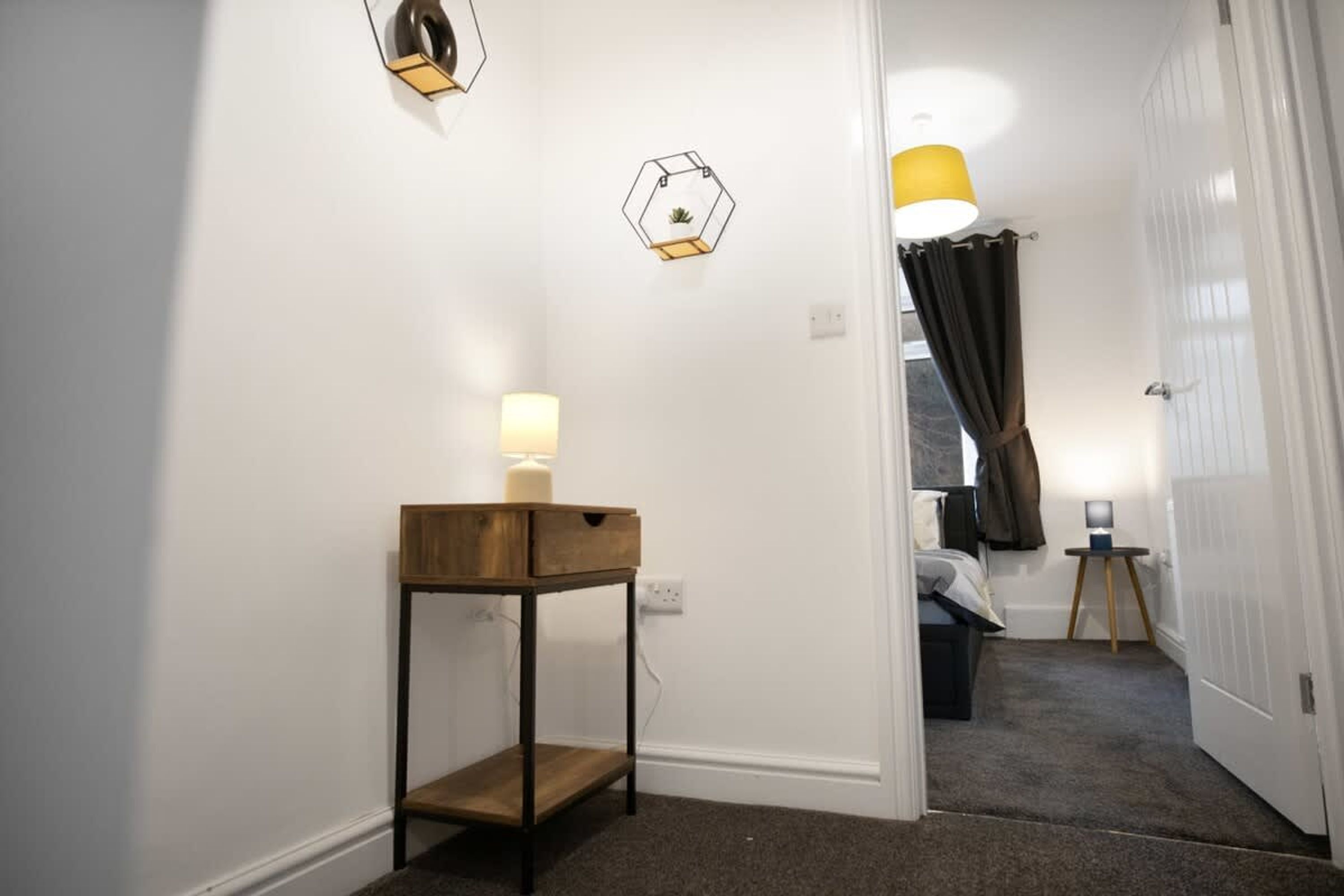 En gang med et træ sidebord, en vægmonteret lampe og en dør, der fører til et soveværelse.