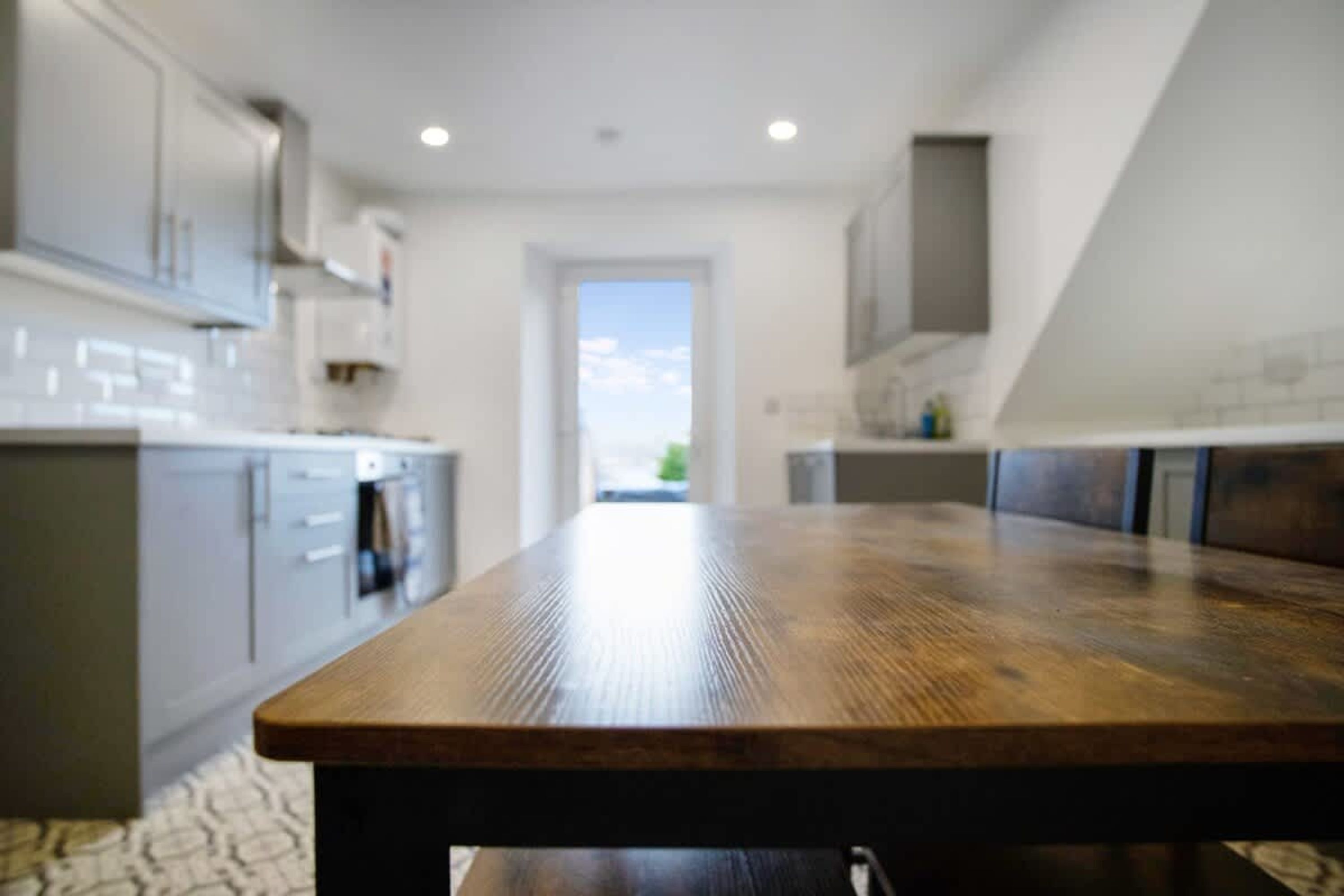Eine moderne Küche mit Esstisch aus Holz, grauen Schränken und Blick durch eine offene Tür.