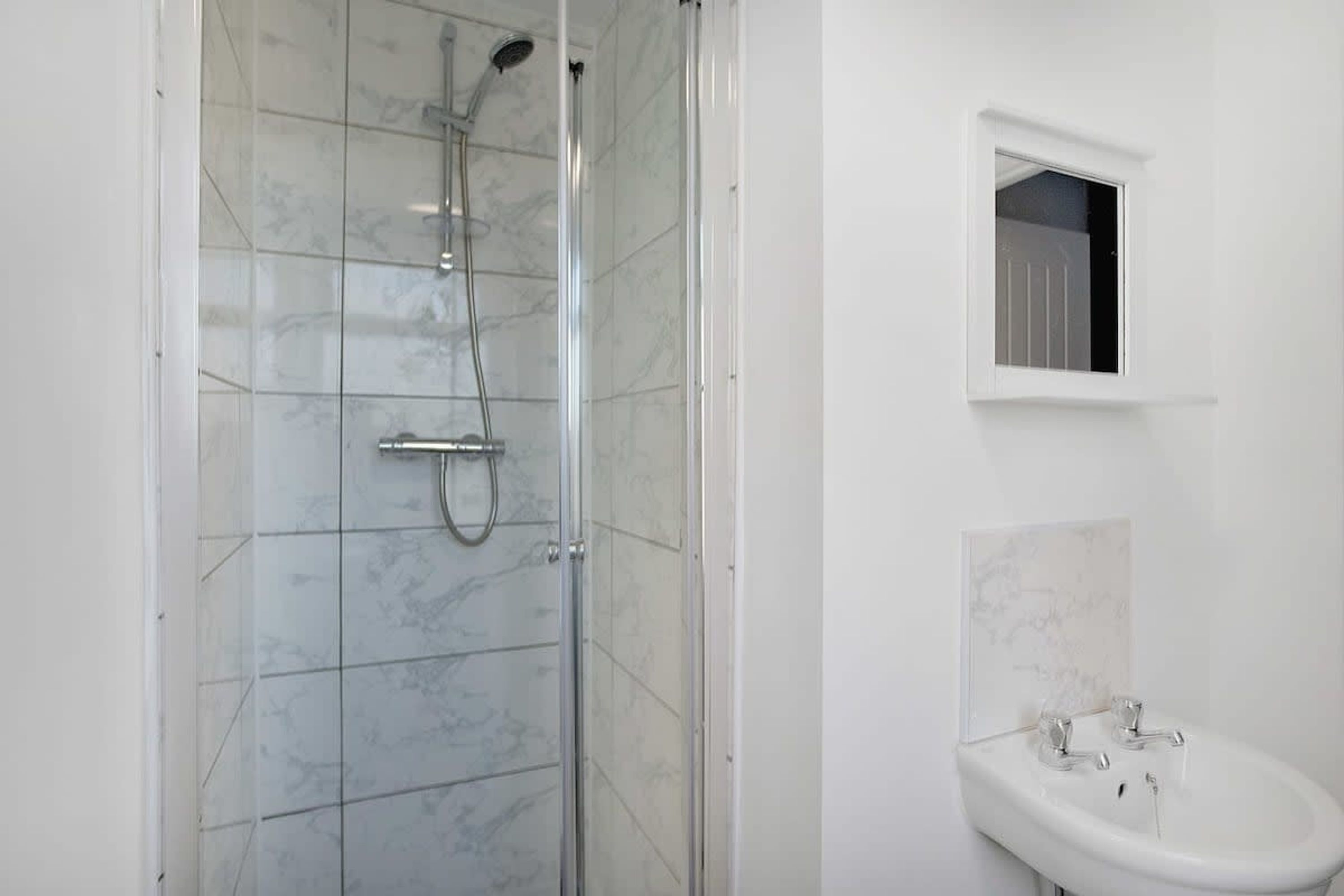 Een badkamer met een douchecabine van glas, een witte wastafel en een klein raam boven de wastafel.