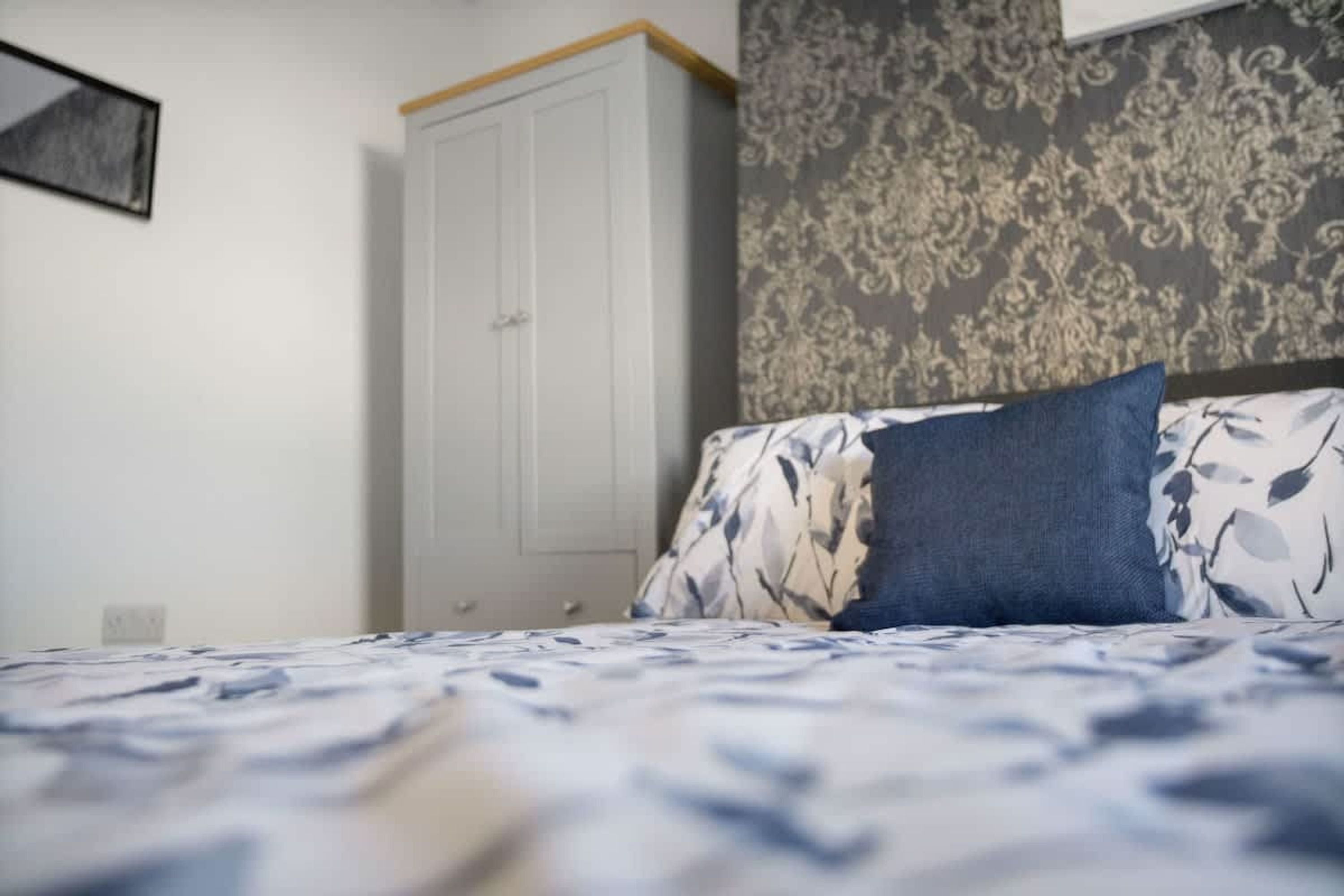 Un dormitorio con cama, armario y papel tapiz estampado.