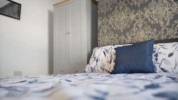 A bedroom with a bed, a wardrobe, and patterned wallpaper.