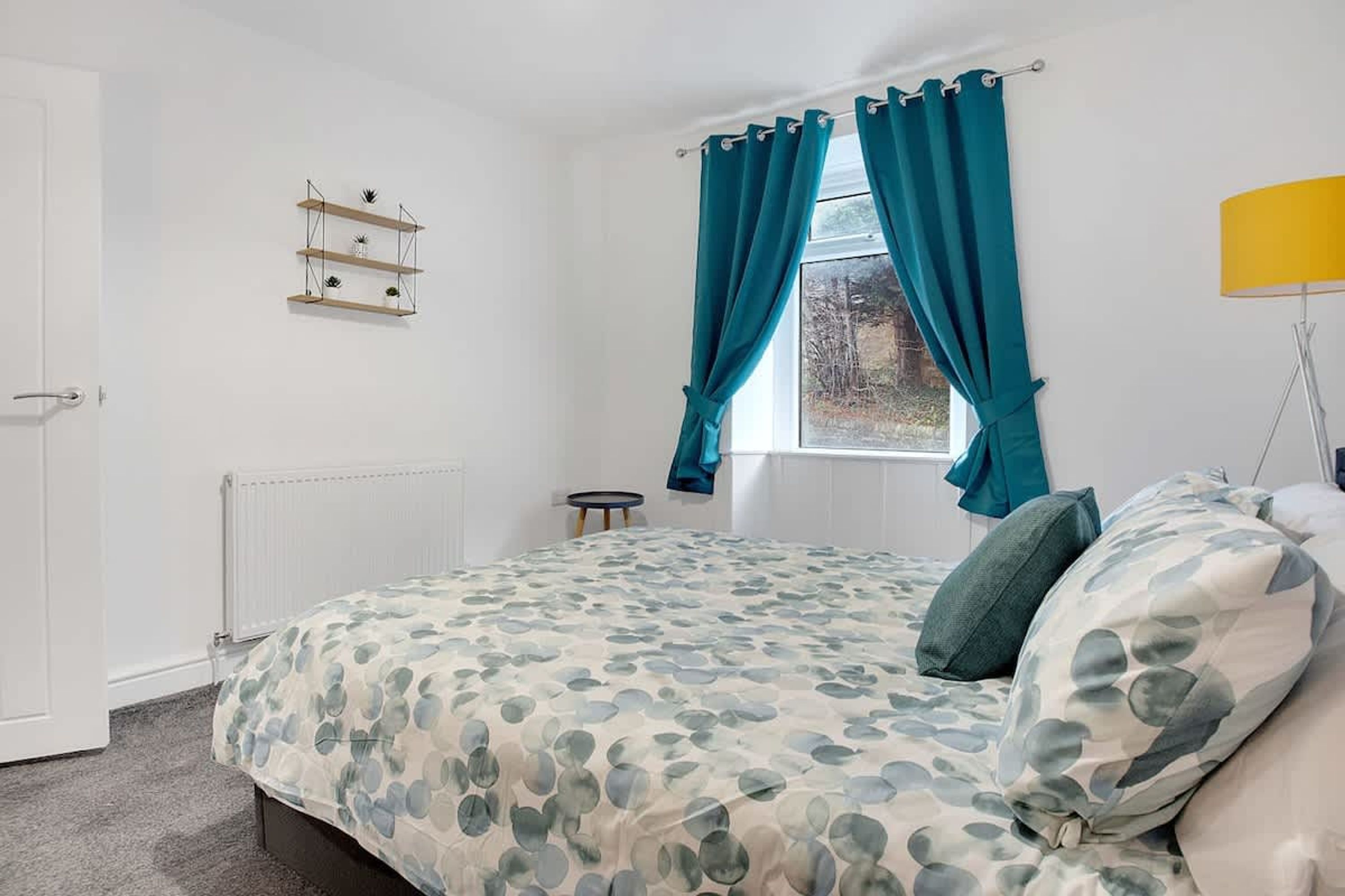 Ein Schlafzimmer mit Bett, Vorhängen an einem Fenster, einer Heizung, einem Regal und einer Lampe.