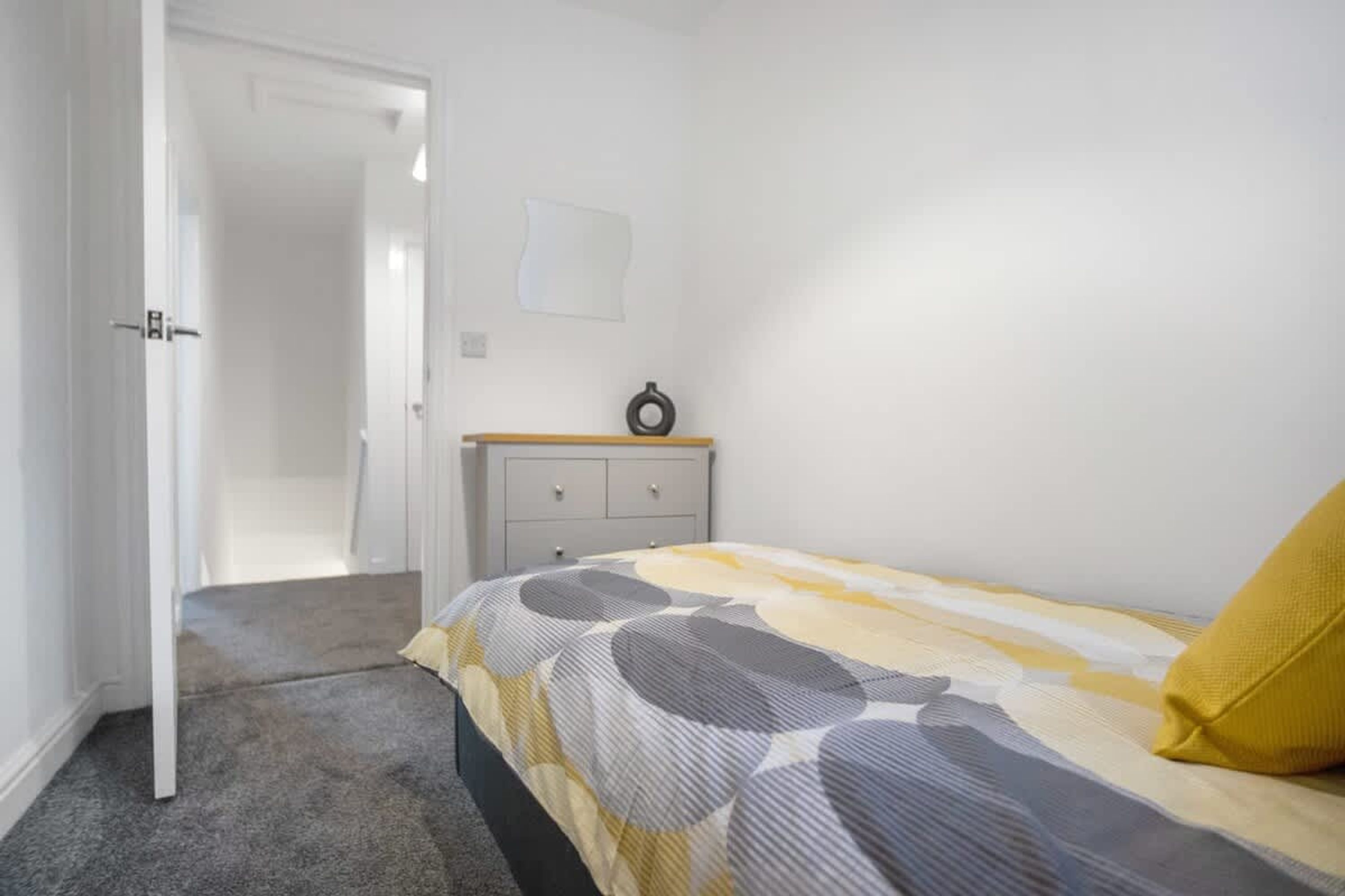 A bedroom with a bed, a bedside table, a wardrobe, and a door leading to another room.