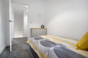 Un dormitorio con cama, mesita de noche, armario y puerta que da a otra habitación.